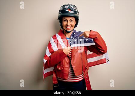 Femme motard d'âge moyen portant un casque de moto et drapeau des états-unis avec le visage surprise pointant du doigt vers lui-même Banque D'Images