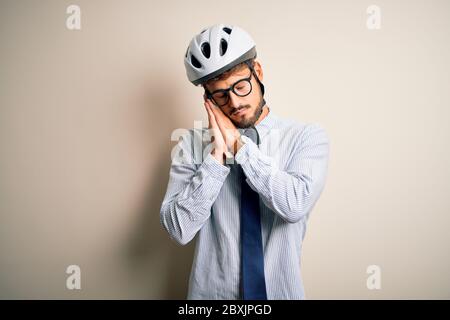 Jeune homme d'affaires portant des lunettes et un casque de vélo debout sur bakground blanc isolé dormant fatigué rêvant et posant avec les mains ensemble pendant Banque D'Images