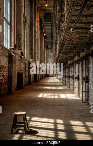 Tabouret assis dans le couloir d'une prison abandonnée, avec des ombres sur le sol des barres dans les fenêtres. Banque D'Images