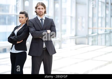 Homme d'affaires et femme professionnels debout dos à dos dans le bureau regardant la caméra. Banque D'Images