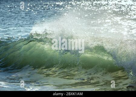 La lumière du soleil brille à travers des vagues qui s'écrasent sur une plage, en les transformant en couleurs vertes et dorées. Photo prise à la plage de Papohaku, à Molokai, Hawaï. Banque D'Images