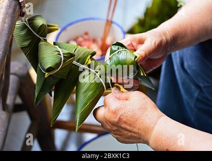 Deux mains serrer la ficelle sur la feuille pour faire Zong ZI, boulettes de riz chinois pour le festival des bateaux-dragons (Festival Duanwu). Banque D'Images