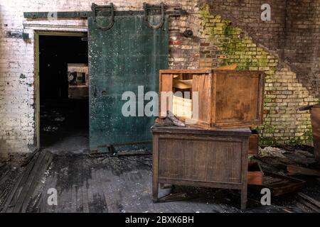 Intérieur d'une chambre avec un vieux bureau, caisse cassée, murs de briques moeuses, et une porte verte intéressante. Banque D'Images