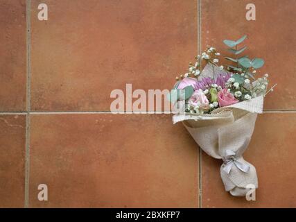 Le bouquet de fleurs à la main se compose de chrysanthème, de roses et de feuilles vertes. Sur fond de mosaïque orange. Vue de dessus. Banque D'Images