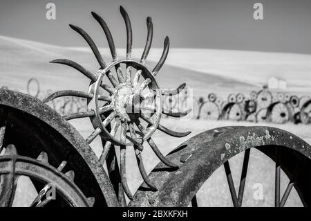 Image infrarouge d'une clôture en vieilles roues rouillées en métal. Des collines ondoyantes et un ciel nuageux sont en arrière-plan avec une grange blanche. Banque D'Images