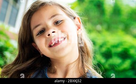 Une jeune fille de sept ans à l'extérieur lors d'une journée ensoleillée souriant et regarder dans l'appareil photo Banque D'Images