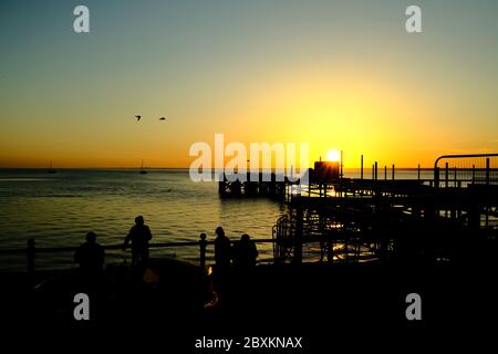 Vue sur Solent jusqu'au continent sur Totland Pier isle of Wight au coucher du soleil yachts kayakistes en bord de mer silhouette orange phosphorescente Banque D'Images