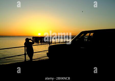 Vue sur Solent jusqu'au continent sur Totland Pier isle of Wight au coucher du soleil avec des photographes et leurs véhicule en silhouette de premier plan Banque D'Images