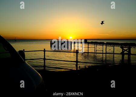 Vue sur Solent jusqu'au continent sur Totland Pier isle of Wight au coucher du soleil yacht mouette lueur orange crépuscule Banque D'Images