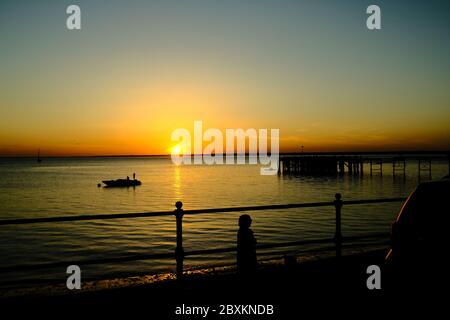 Vue sur Solent jusqu'au continent sur Totland Pier isle of Wight au coucher du soleil avec yacht hors-bord ancré et des kayakistes en silhouette Banque D'Images