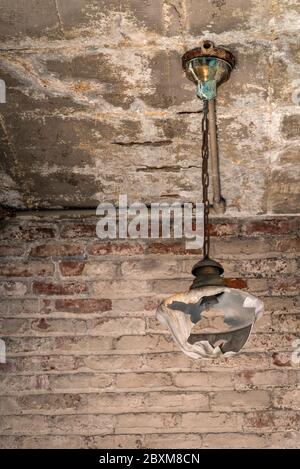 Luminaire cassé suspendu contre un mur de briques avec peinture écaillée. Image prise à l'ancienne usine de dentelle de Scranton, démolie en 2019. Banque D'Images