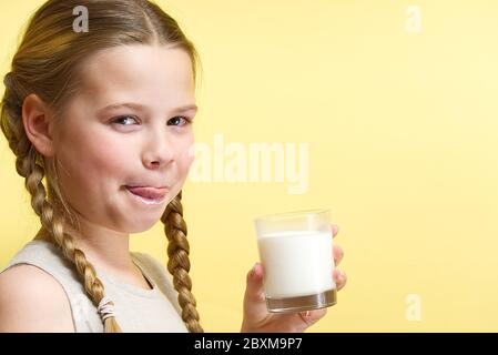 une fille avec des queues de porc et une moustache au lait boit du lait sur fond jaune Banque D'Images