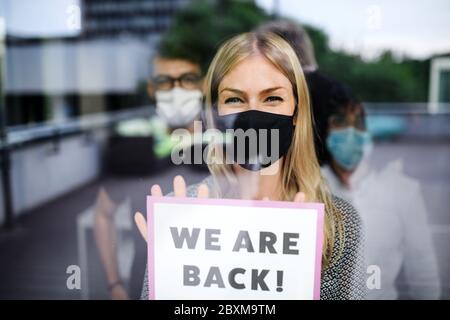 Femme avec masque de visage au travail au bureau après le verrouillage, nous tenant signe de dos. Banque D'Images