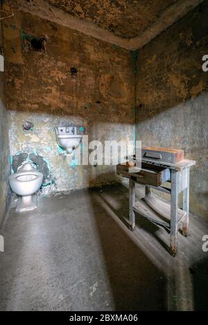 Intérieur d'une cellule dans une prison abandonnée avec de vieux toilettes, lavabo et bureau. Banque D'Images