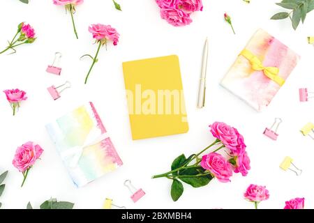 Composition féminine avec carnet, cadeau et fleurs roses sur fond blanc. Pose à plat. Banque D'Images
