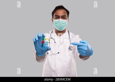 Médecin pointant vers une boîte de Petri portant un masque médical et des gants isolés. Médecine, concept de la science Banque D'Images