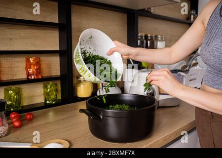 La femme prépare une salade d'herbes vertes à l'aide d'aneth et de persil dans une cuisine moderne en bois. Style de vie sain Banque D'Images