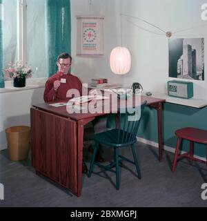 Dans les années 1950. Un homme à un bureau organise ses tirages photographiques et les place dans un album photo. Son appareil photo est visible à côté de lui. C'était analogique et on pouvait prendre des photos en couleur et en noir et blanc. Pour les photos en noir et blanc, le film était négatif et a été ensuite copié sur des tirages photographiques. Suède 1968. Réf. CV45-2 Banque D'Images