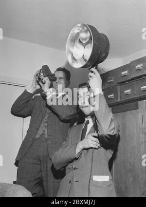 Tournage dans les années 1950. Un homme tourne avec une petite caméra de 8 mm tandis que son ami tient des lampes pour éclairer le sujet filmé. La caméra a produit un film analogique qui a été visionné sur un écran blanc par un projecteur. Suède 1958 Banque D'Images