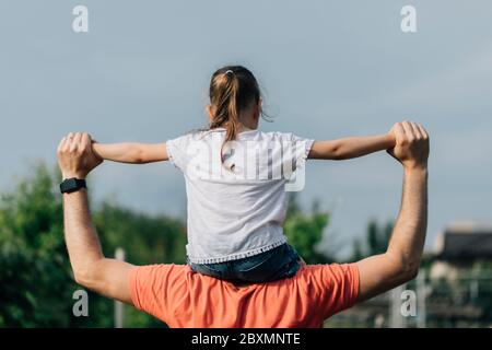 Père tenant sa fille sur les shouldders et debout sur fond d'été nature. Concept de famille ou de fête des pères. Vue arrière. Banque D'Images