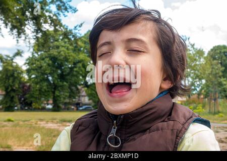 Portrait d'un jeune garçon avec ses yeux fermés et la bouche ouverte pris au milieu du rire pris à l'extérieur dans le parc local Banque D'Images