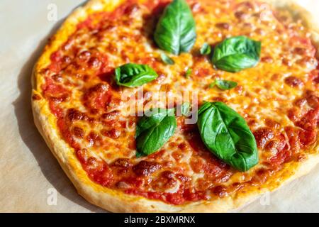 Gros plan vue panoramique peu profonde de la savoureuse pizza italienne cuite maison à la Margarita sur du papier de cuisson juste préparé au four. Fromage mozzarella fondu Banque D'Images