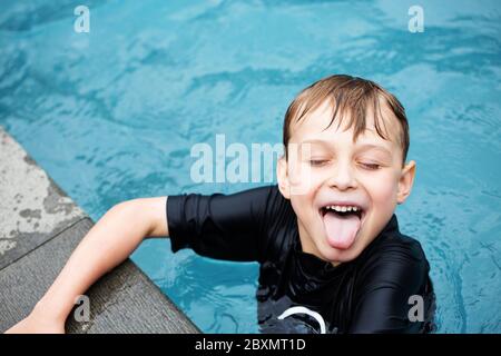 Jeune garçon dans une piscine faisant un visage drôle et collant la langue dehors avec les yeux fermés