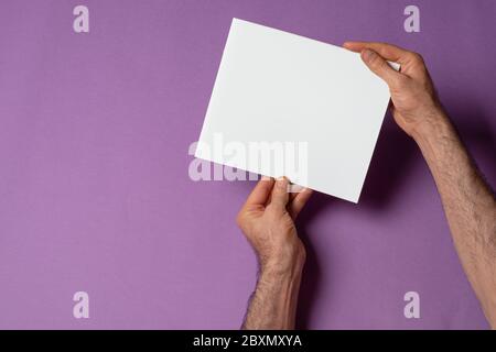 Main masculine tenant un catalogue avec une couverture vierge sur fond violet, modèle de série maquette prêt pour votre conception, chemin de sélection de couverture inclus Banque D'Images