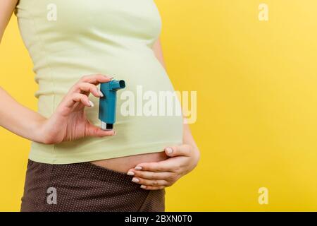 Gros plan de la femme enceinte utilisant l'inhalateur d'asthme pendant l'attaque pour être en bonne santé sur fond coloré avec l'espace de copie. Concept de soins de santé. Banque D'Images