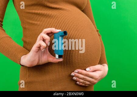 Gros plan de la femme enceinte utilisant l'inhalateur d'asthme pendant l'attaque pour être en bonne santé sur fond coloré avec l'espace de copie. Concept de soins de santé. Banque D'Images