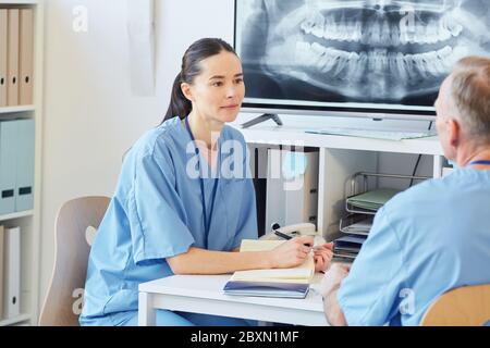 Portrait d'une infirmière féminine portant un uniforme bleu parlant à un collègue tout en étant assise à un bureau dans une clinique de bureau moderne, espace de copie Banque D'Images