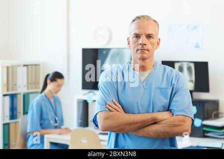 Portrait à la taille du médecin mature et confiant regardant la caméra tout en se tenant debout avec les bras croisés dans l'intérieur moderne de l'hôpital, espace de copie Banque D'Images