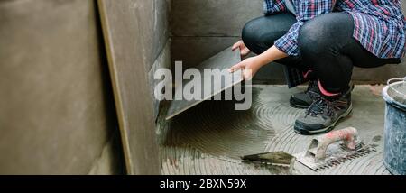 Femme de construction posant un nouveau plancher de carreaux Banque D'Images