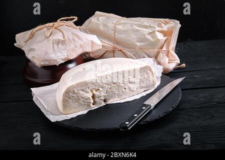 Le fromage géorgien Suluguni est tranché sur une planche de bois sur fond sombre, gros plan, emballage écologique. Photos pour les épiceries Banque D'Images