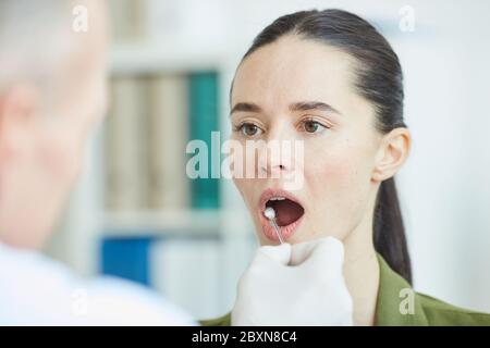 Médecin mâle méconnaissable prenant un échantillon d'écouvillon de la bouche et de la gorge de la jeune femme pour le test de virus en clinique, espace de copie Banque D'Images