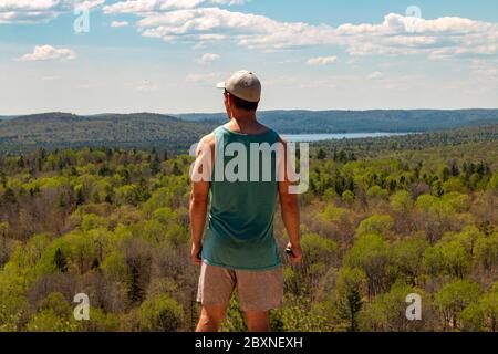 Vue arrière d'un homme assis sur un rocher au-dessus d'un paysage. Banque D'Images