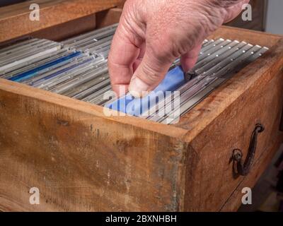 Un homme vérifie les CD d’une collection dans un ancien tiroir en bois et en choisit un à sortir. Banque D'Images