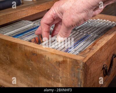 Un homme vérifie les CD d’une collection dans un ancien tiroir en bois et en choisit un à sortir. Banque D'Images