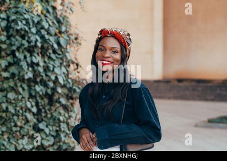 Belle jeune fille musulmane noire africaine portant un bandana dans la rue de la ville moderne. Elle marche en jeans blancs avec un sourire heureux sur son visage. FAS Banque D'Images