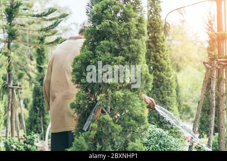 Un homme âgé en quarantaine porte un masque facial pour empêcher la propagation du virus Corona (Covid-19) arroser des plantes pour faire de l'exercice dans le jardin à la maison. Ne Banque D'Images