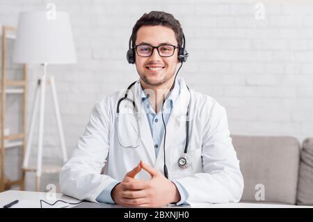 Conférence médicale ou consultation en ligne. Jeune médecin souriant dans des lunettes avec casque Banque D'Images