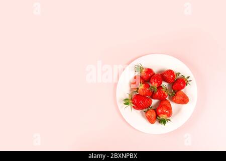 Vue de dessus fraise dans une assiette blanche sur fond rose, espace horizontal pour le texte Banque D'Images