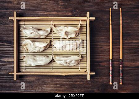 vue de dessus d'un plateau en bambou avec gyozas, sur la table en bois sombre il y a quelques baguettes, concept de la restauration rapide orientale saine Banque D'Images