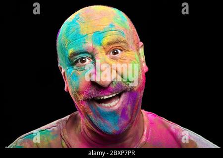 Un homme heureux recouvert de poudre Holi aux couleurs vives pour célébrer le Festival des couleurs en regardant l'appareil photo rire dans un portrait de gros plan isolé sur Banque D'Images