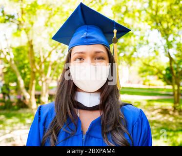 Jeune fille d'université en chapeau et robe ayant son portrait pris avec masque de visage pendant la pandémie de coronavirus Banque D'Images