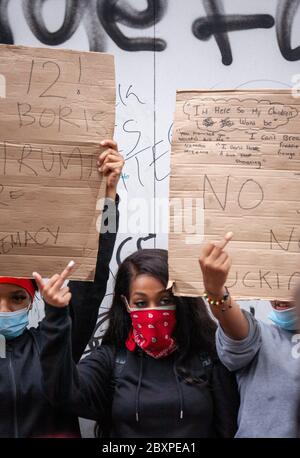 Groupe de trois femmes, portant un masque facial, tenant des signes et montrant le signe du milieu de la protestation du BLM UK. Londres, Angleterre Royaume-Uni Banque D'Images