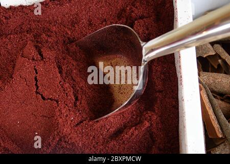 Les baies de Sumac rouges épiment dans une boîte blanche avec une grande pelle en métal, vue de dessus, foyer sélectif, faible profondeur de champ, macro. Épice oriental exotique. Arom Banque D'Images