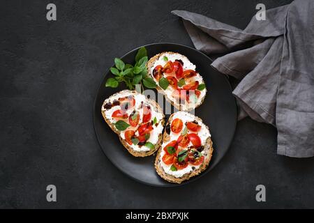 Bruschetta italienne au ricotta, tomates cerises, vinaigre balsamique sur plaque noire, fond en béton noir. Espace de copie de la vue de dessus pour le texte ou D Banque D'Images