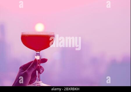 Cocktail en verre violet et rouge style pop art à la main avec vue panoramique sur la ville en toile de fond Banque D'Images