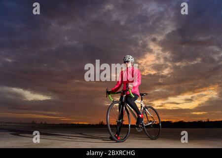 Portrait de jeune cycliste avec vélo de route au coucher du soleil. Concept de style de vie sain et de sport de plein air. Banque D'Images